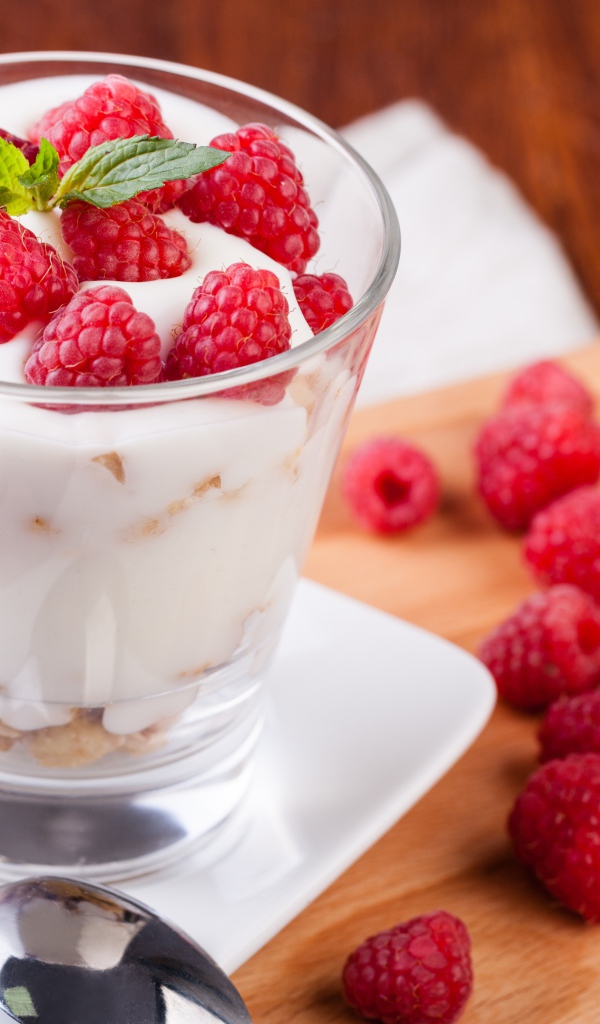 Десерт с йогуртом и свежей малиной в стеклянном стакане на столе