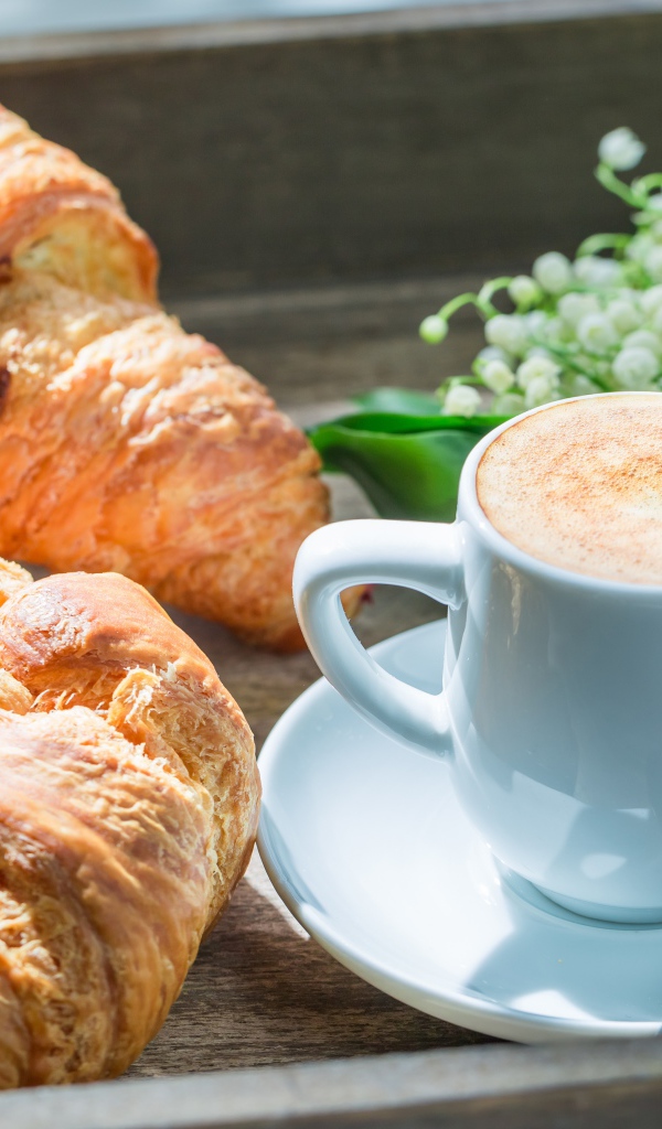 Свежие круассаны с чашкой кофе и букетом ландышей на столе