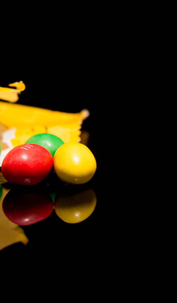 Разноцветные конфеты  M&m's отражаются в черной поверхности стола 