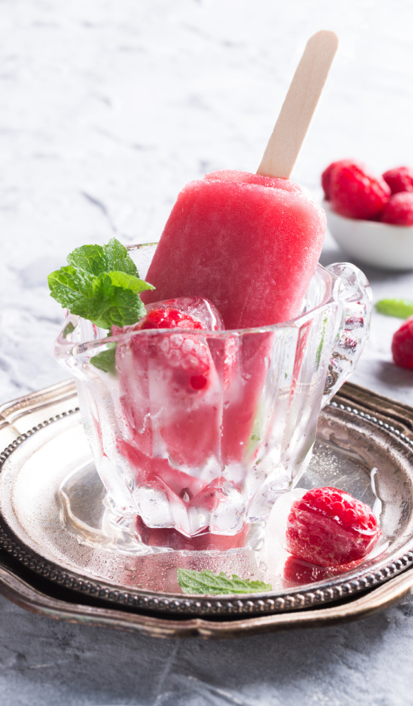 Малиновое мороженое на палочке в стеклянном стакане на столе со свежими ягодами