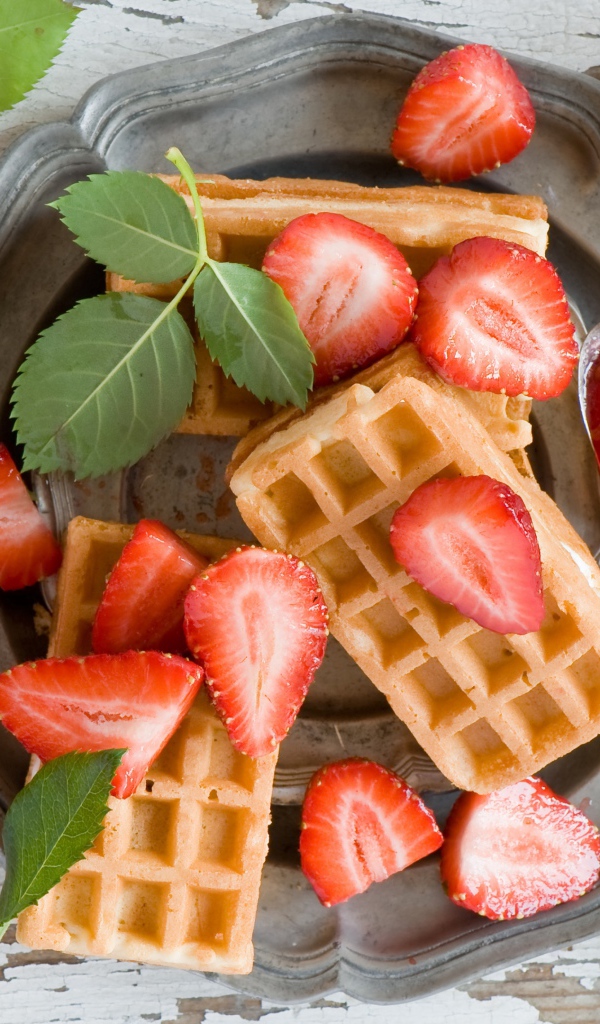 Сладкие вафли со свежей клубникой и красными розами на столе