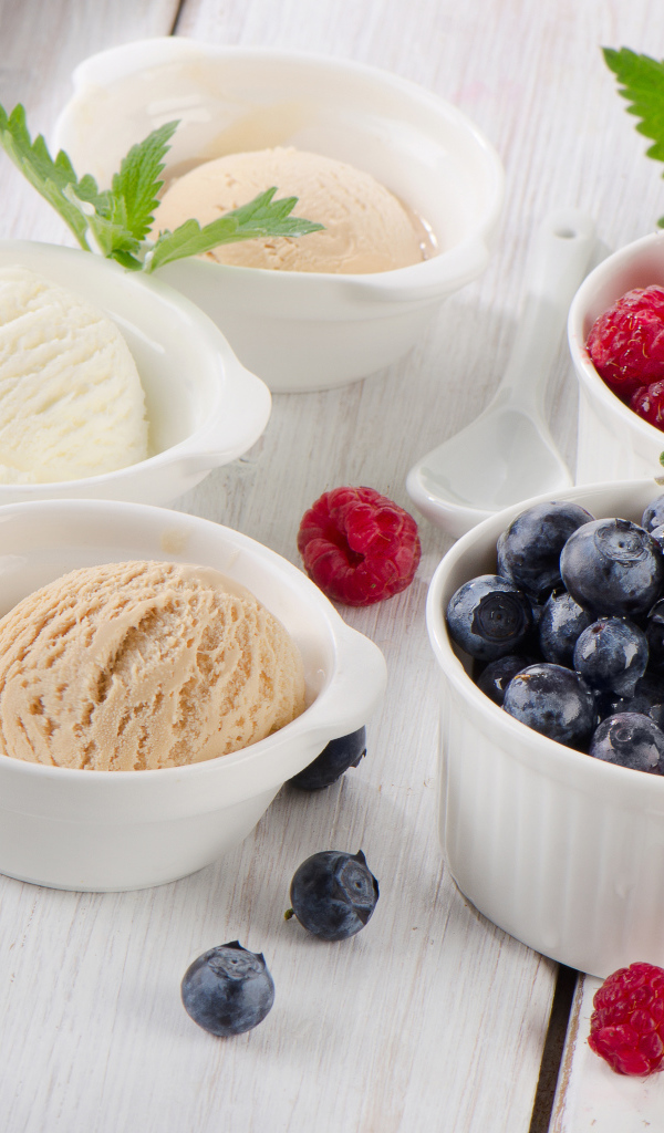 Три шарика мороженого и свежие ягоды малины и черники в белых тарелках