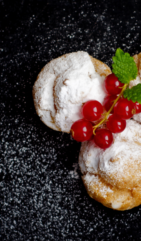 Три пирожных с сахарной пудрой и красной смородиной на черном фоне