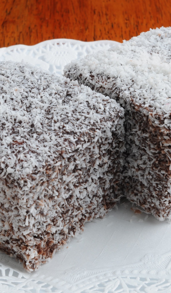 Два кусочка пирожного в кокосовой стружке на белой тарелке