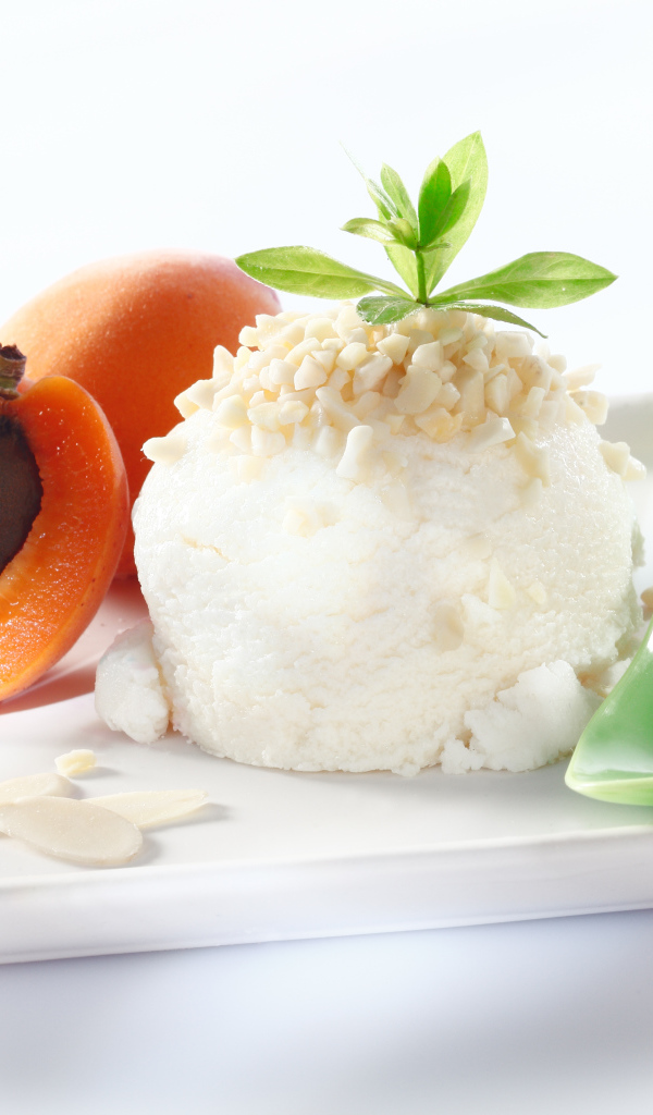 Шарик ванильного мороженого с абрикосами на белой тарелке с ложкой