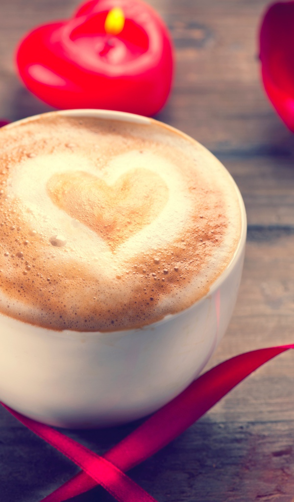 Чашка кофе на столе с красной свечой и лентой