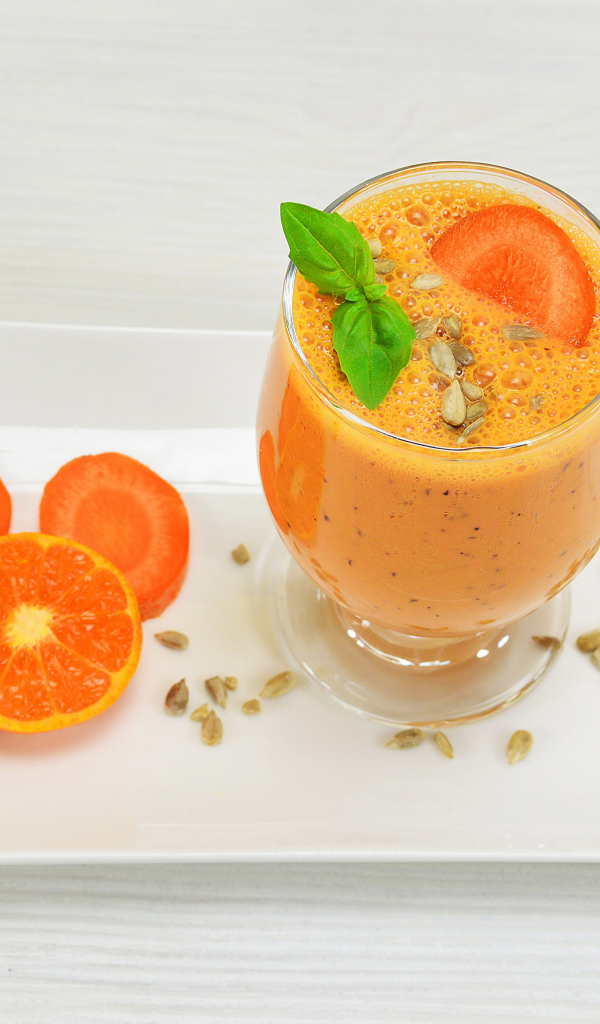 Бокал морковного коктейля с апельсином на белой тарелке