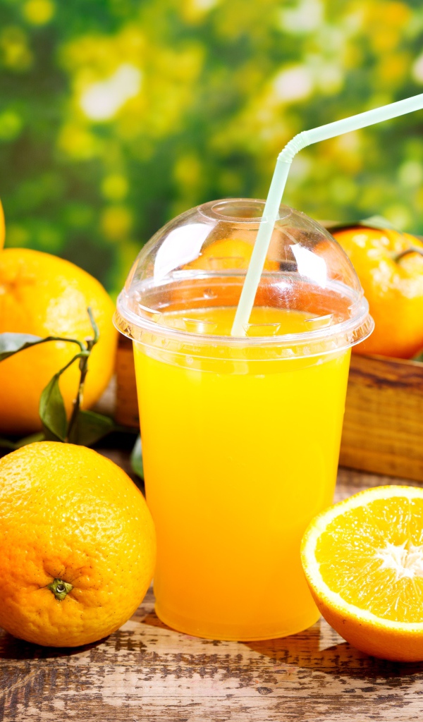 Стакан апельсинового сока с трубочкой на столе со свежими апельсинами