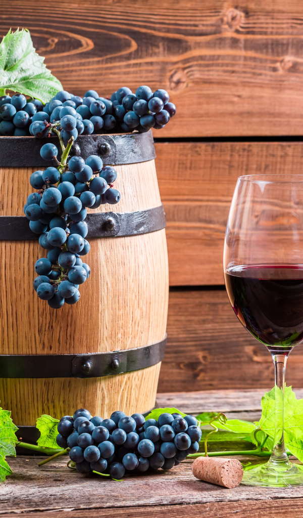Бокал вина с бочкой и бутылкой на столе с гроздьями синего винограда с листьями