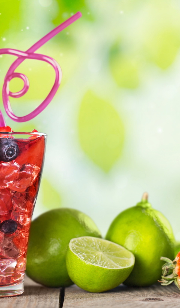 Коктейль с клубникой и ягодами черники в стакане со льдом на столе с лаймами и клубникой