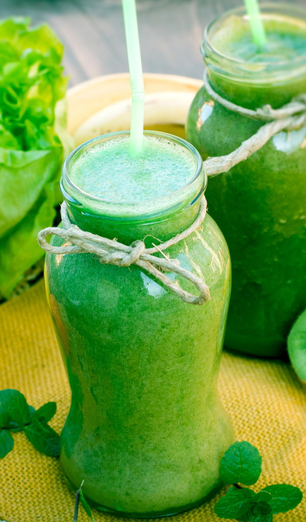 Зеленый смузи в бутылках с трубочками и фруктами на столе