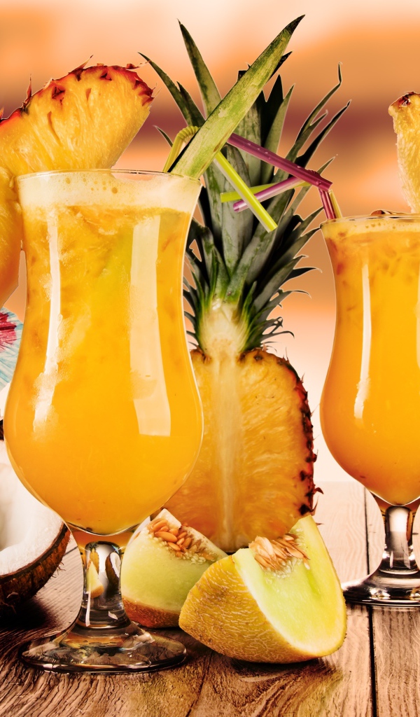 Тропические коктейли на столе со свежими ананасом, кокосом и кусочками дыни
