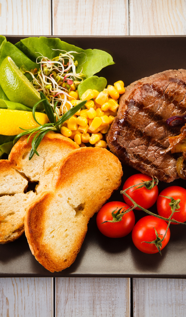 Аппетитный кусок жареного мяса на тарелке с овощами и гренками