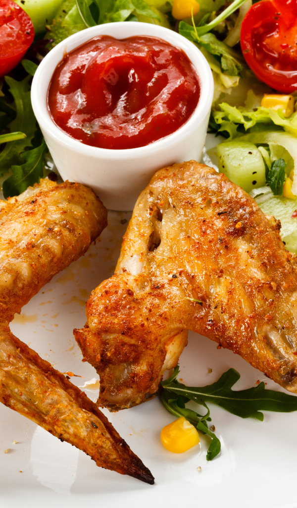 Жареные куриные крылышки с овощами и кетчупом на белой тарелке