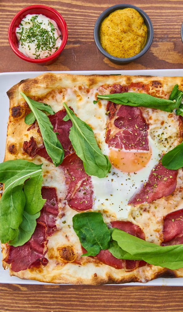 Pizza with bacon and green basil leaves on a table