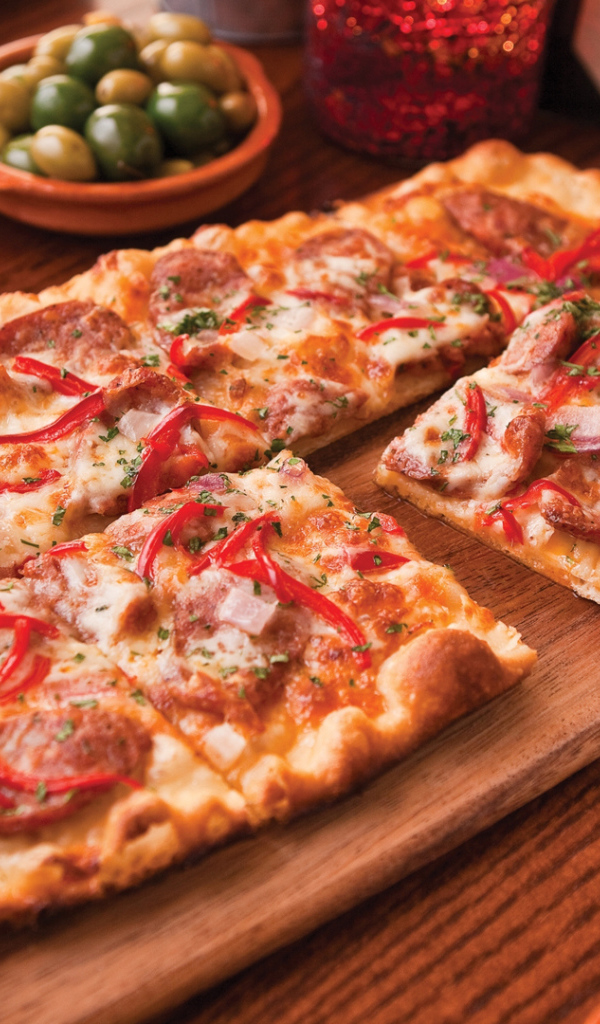 Порезанная на кусочки пицца лежит на разделочной доске