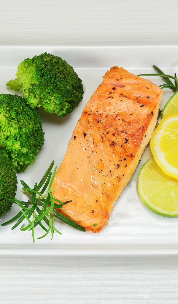 Красная рыба на белой тарелке с лимонами и брокколи