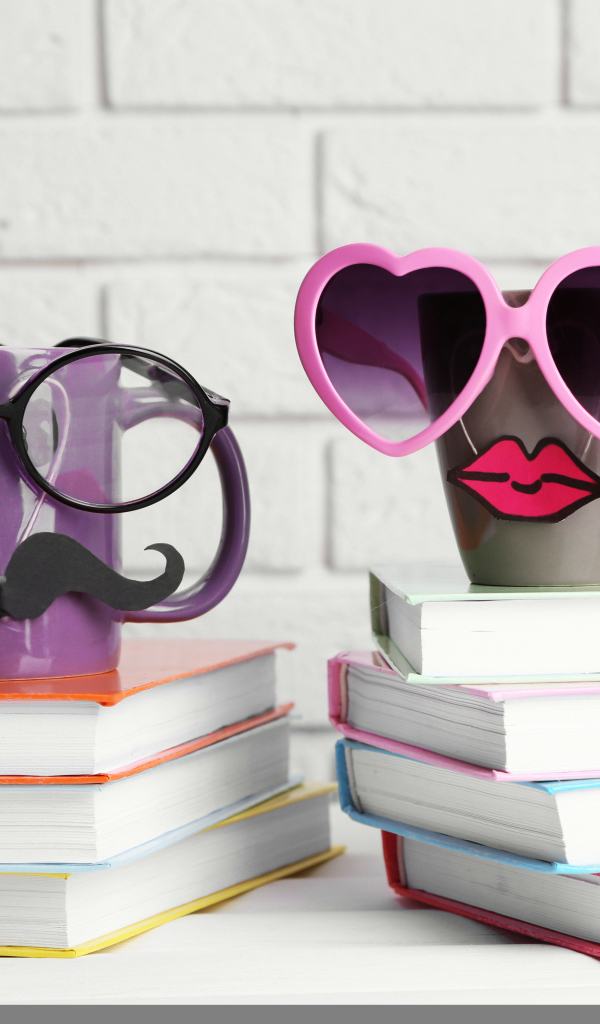 Две забавные чашки в очках стоят на книгах