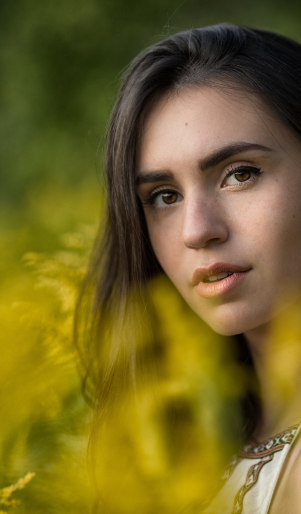 Красивая девушка с нежным взглядом сидит у желтых цветов