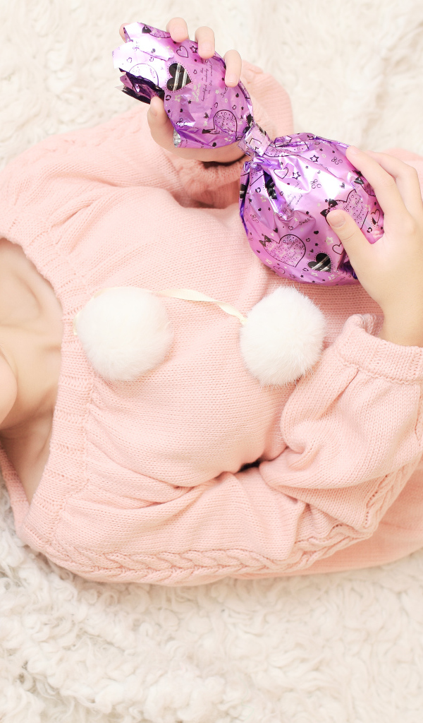 Молодая девушка азиатка в розовом свитере с большой конфетой в руках