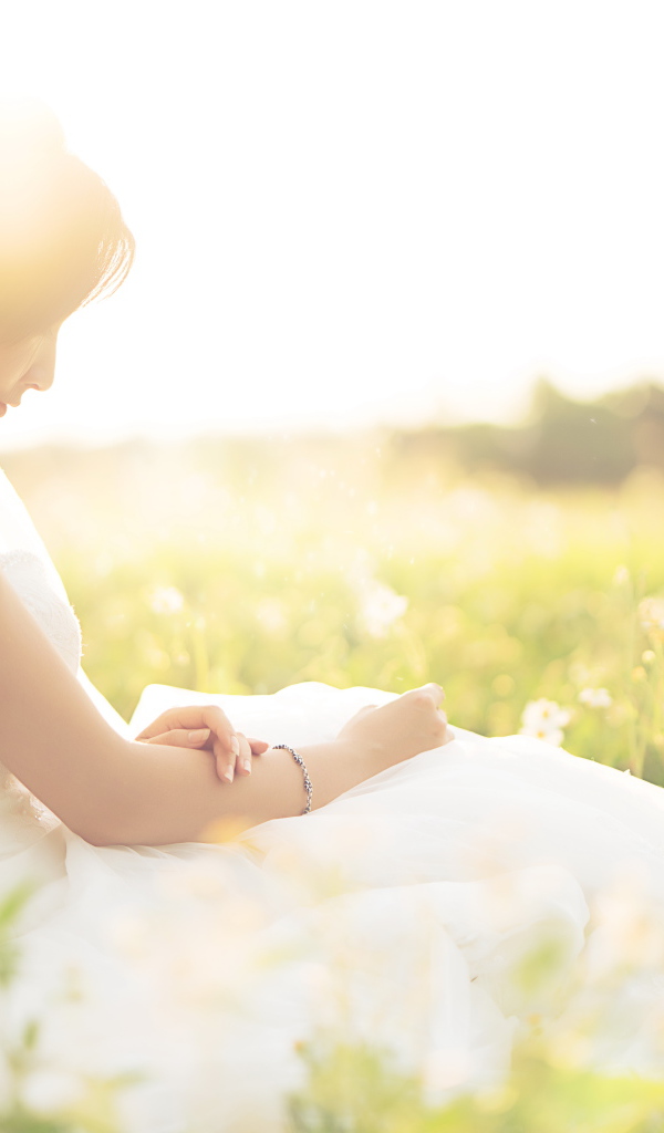 Девушка азиатка в платье невесты сидит на траве в поле 