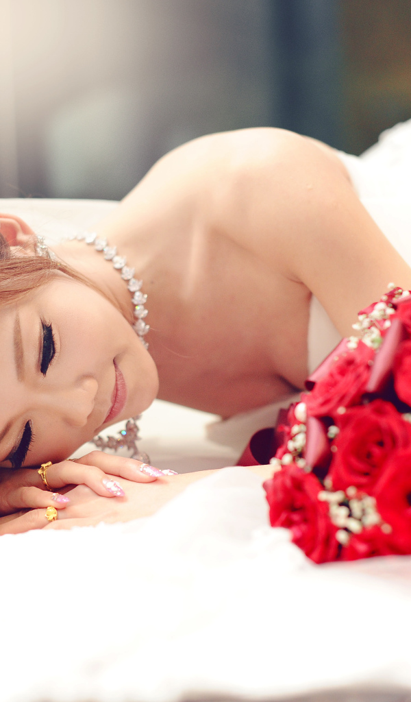 Красивая девушка азиатка в свадебном платье с букетом красных роз