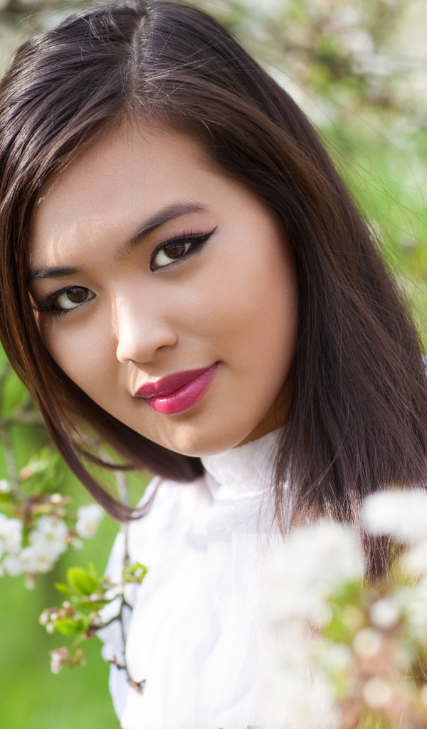 Красивая девушка азиатка в ветках цветущего дерева