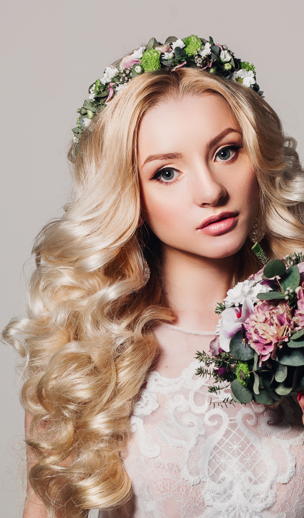 Красивая блондинка в свадебном платье с букетом цветов на сером фоне