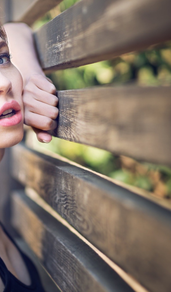 Красивая голубоглазая девушка у деревянного забора 