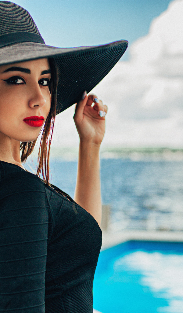 Красивая девушка в большой черной шляпе у бассейна