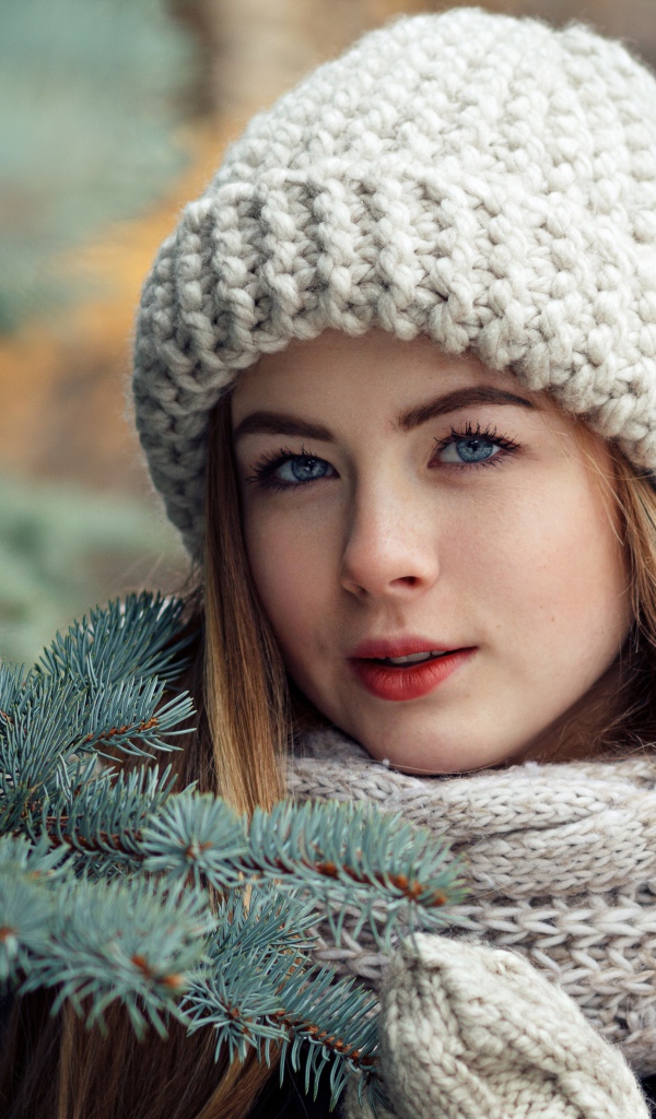 Красивая молодая голубоглазая девушка у еловой ветки зимой