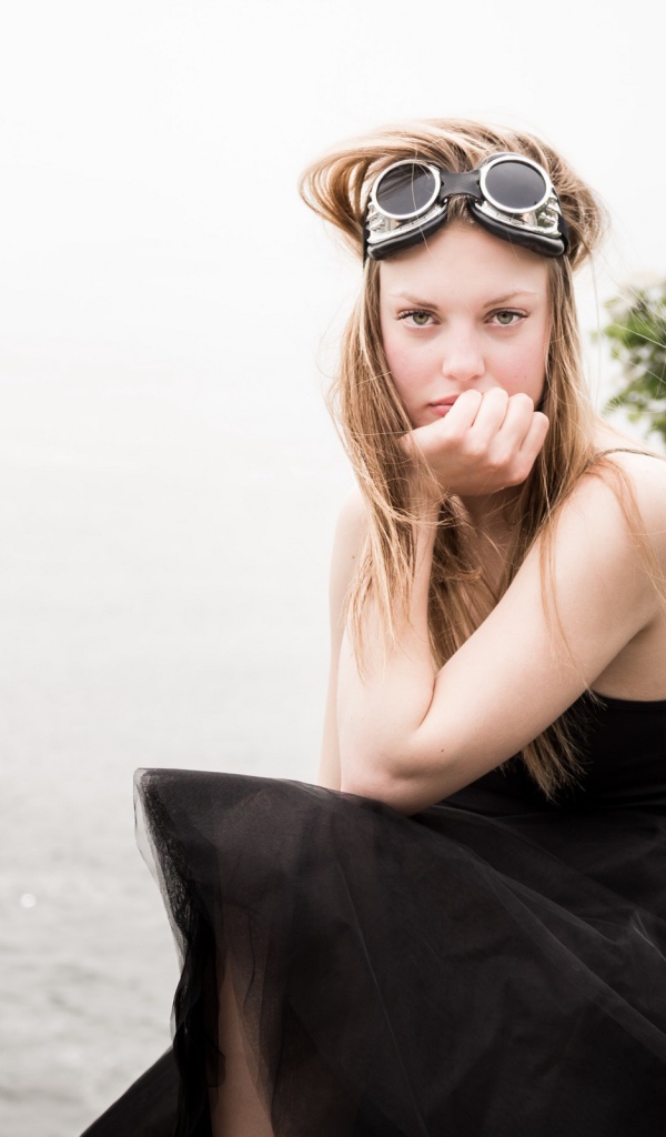 Девушка блондинка с очками на голове сидит на камне