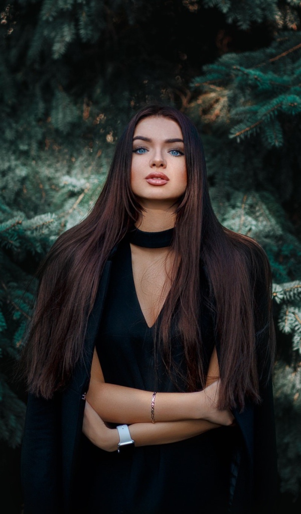 Голубоглазая девушка брюнетка у большой зеленой ели 