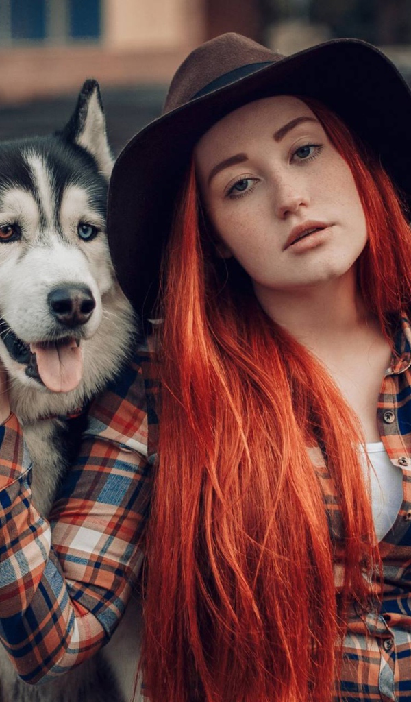Рыжеволосая девушка в черной шляпе сидит с хаски