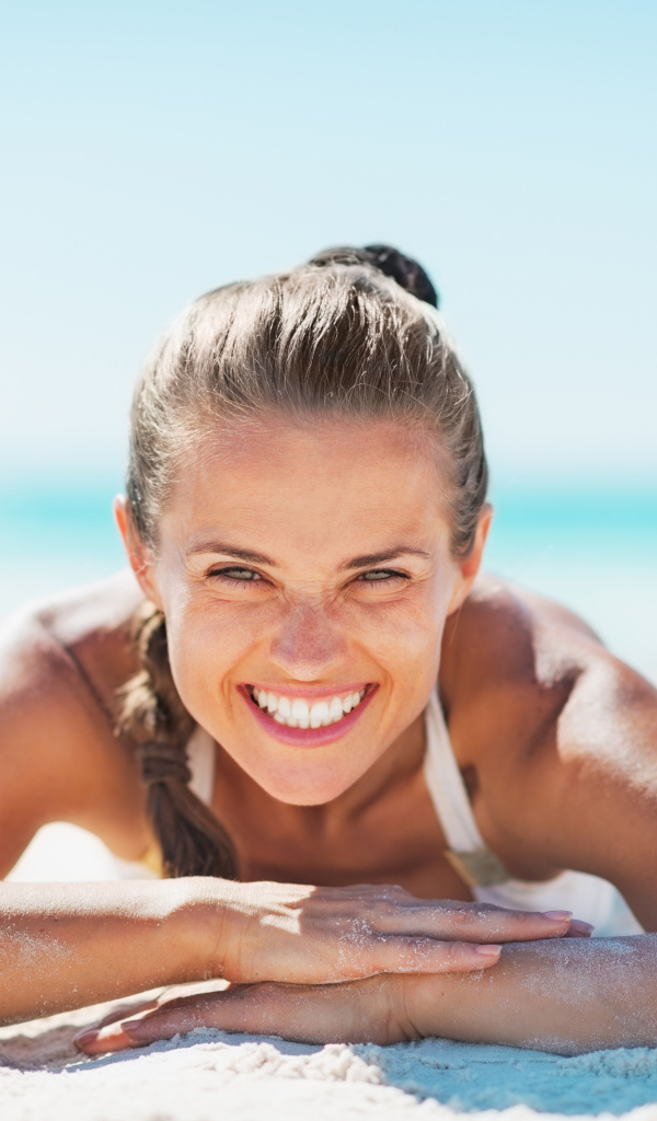Улыбающаяся девушка лежит на белом песке на пляже