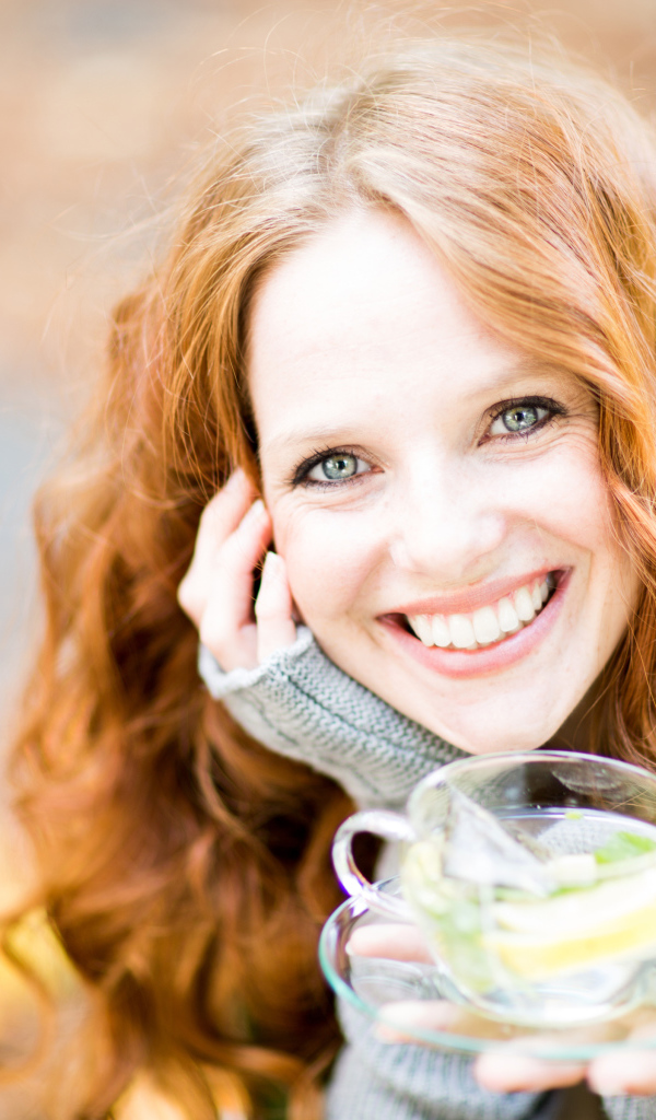 Улыбающаяся рыжеволосая девушка с чашкой чая в руке