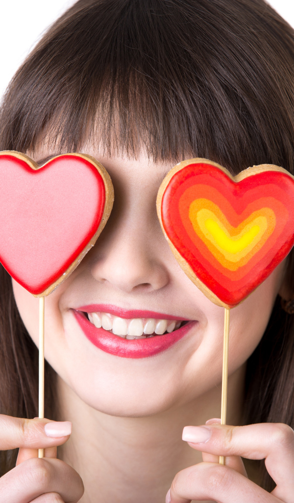 Красивая девушка шатенка закрыла глаза леденцами в форме сердца
