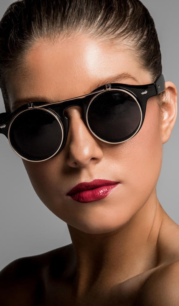 Лицо девушки в черных очках на сером фоне