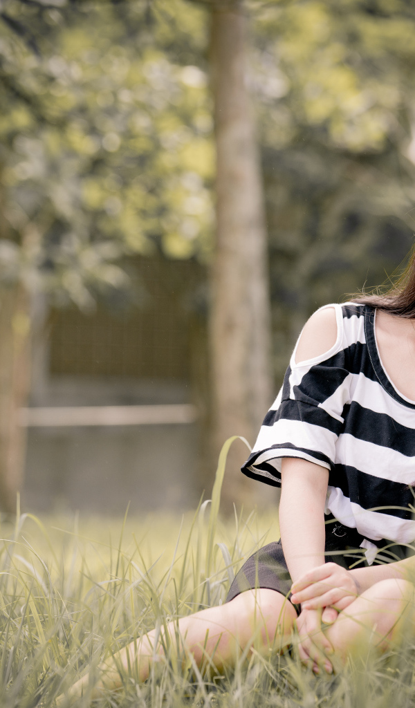 Молодая девушка азиатка сидит на траве у дерева