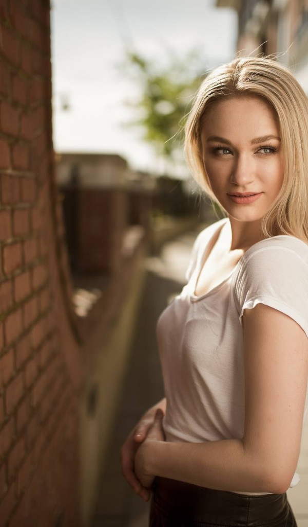 Молодая девушка блондинка у кирпичной стены 