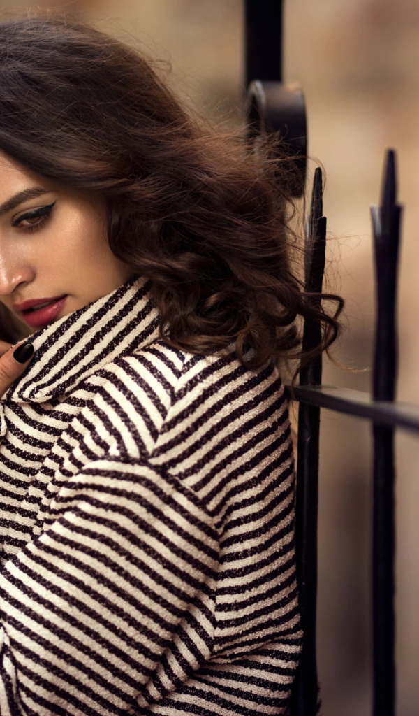 Молодая брюнетка в пальто у забора