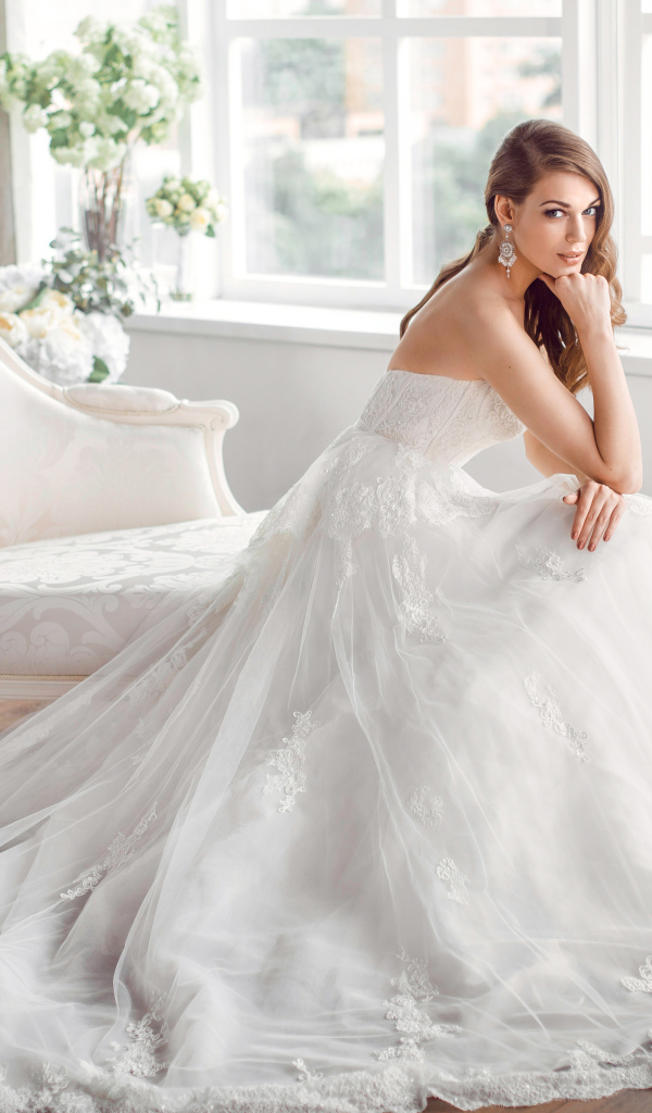 Молодая девушка в красивом свадебном платье сидит в белом кресле