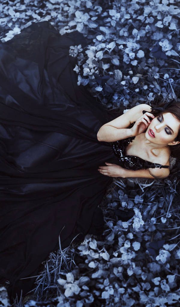 Молодая девушка модель с красивом черном платье лежит на траве