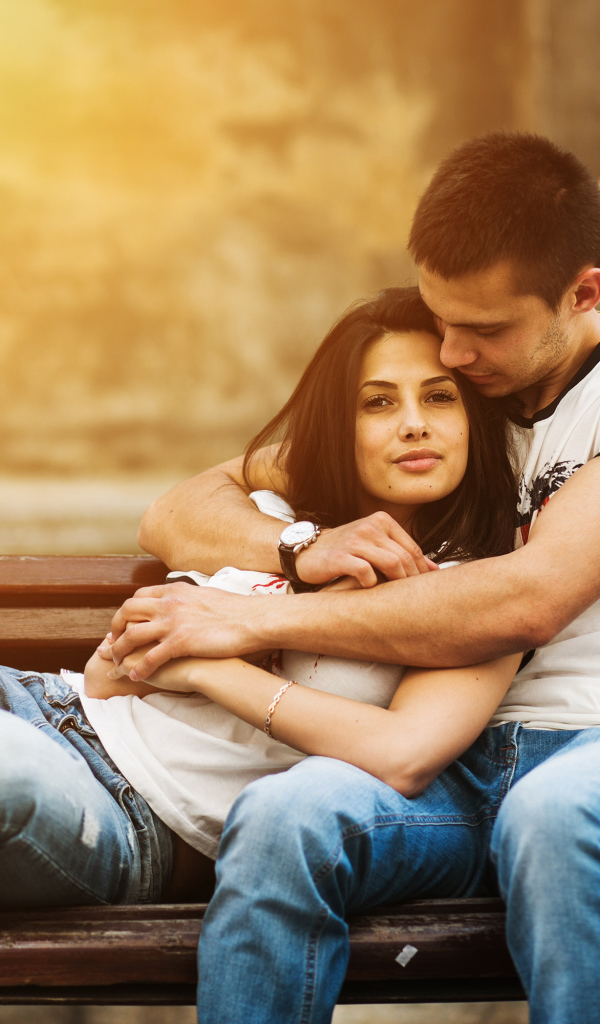 Влюбленная пара сидит на деревянной лавке в парке