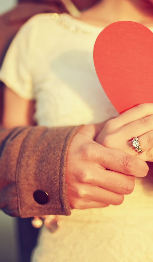 Влюбленная пара держит в руках красное бумажное сердце