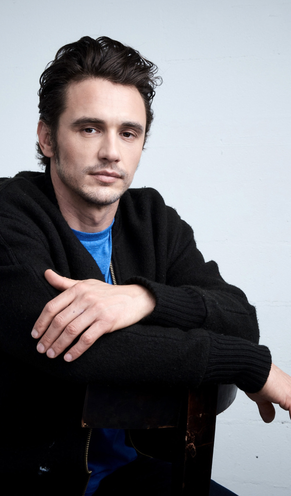 Актер Джеймс Франко в черной кофте на сером фоне