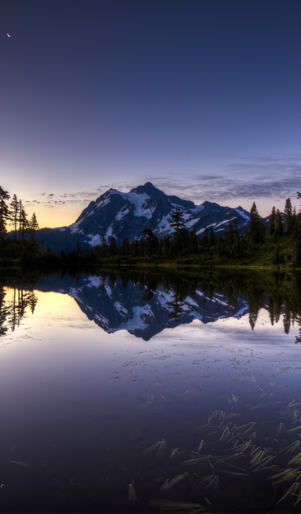 Заснеженная гора и лес отражается в озере вечером