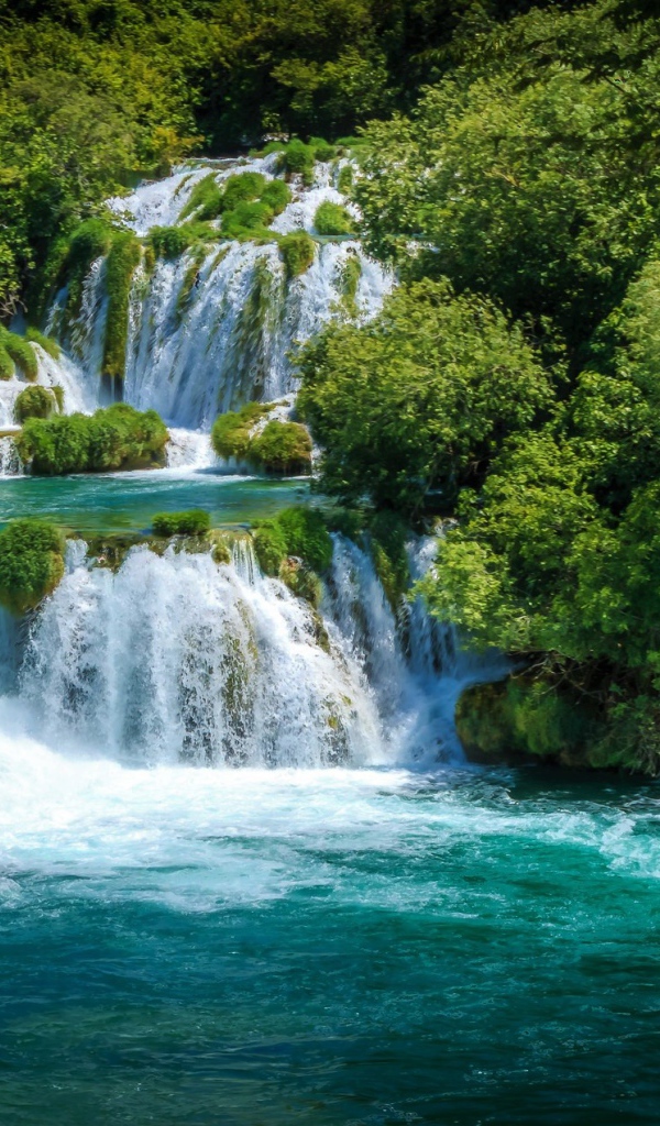 Бушующая голубая вода водопада у зеленых деревьев