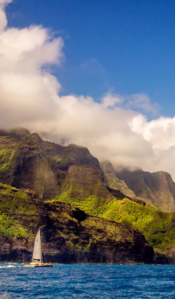 Парусная лодка плывет по голубой воде на фоне покрытых зеленью гор