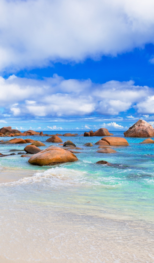 Большие камни на белом песке у голубой воды океана